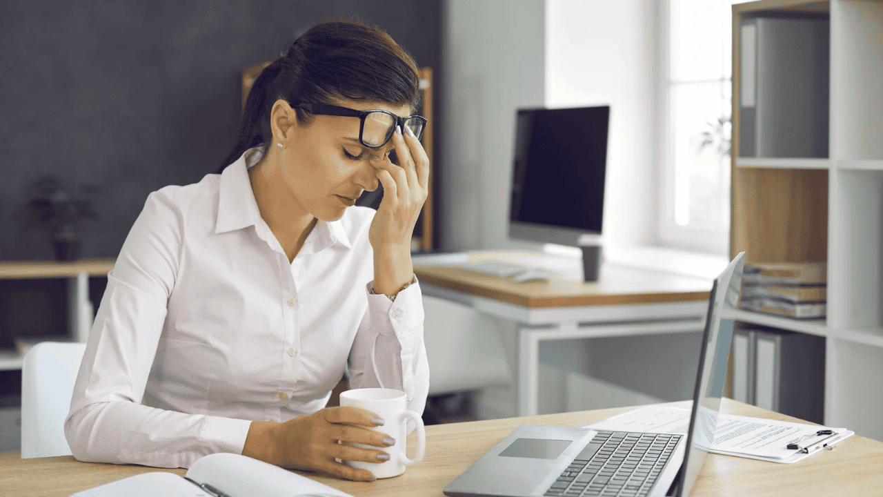 Office woman feeling tired and stressed while working on a laptop, holding a coffee mug and touching her forehead.ఎందుకు ప్రతిరోజూ అలసటగా ఫీల్ అవుతున్నాం? అసలు నిజమైన10 కారణాలు,